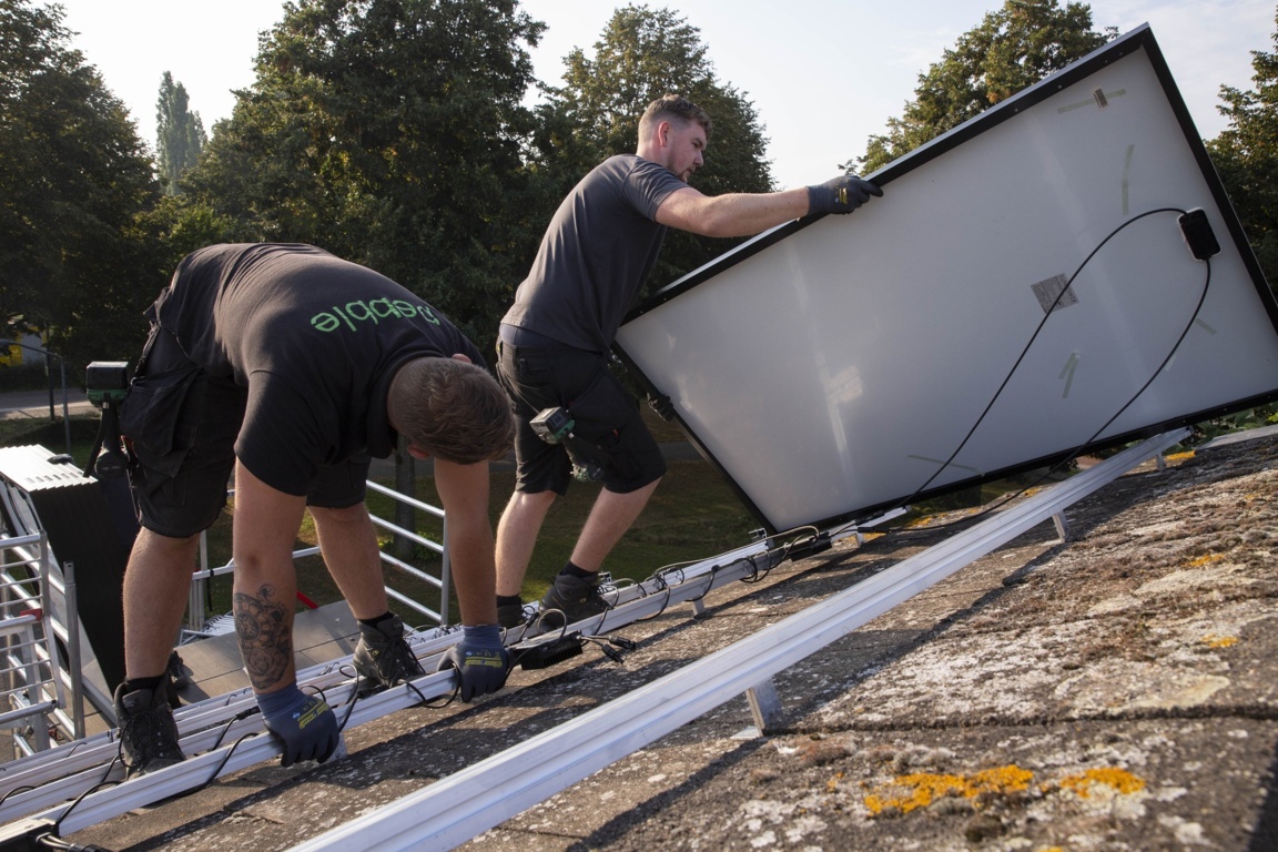 Installateurs van zonnepanelen die op een dak bezig zijn met het monteren van een zonnepaneel op een installatie