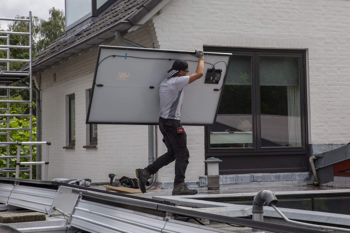 Installateur van zonnepanelen die loopt op een dak met een zonnepaneel in zijn armen