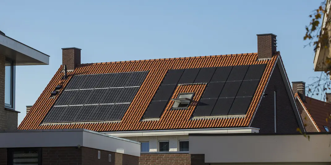 Een hellend dak met zonnepanelen erop en een strak blauwe lucht op een zonnige dag