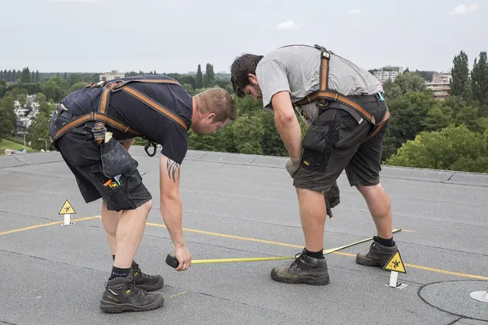 Twee installateurs van zonnepanelen op een dak aan het meten voor het montageframe van de zonnepanelen