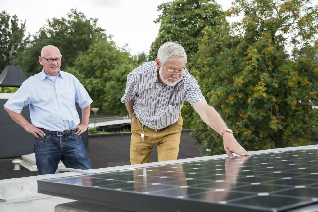 Een tevreden klant die voelt aan zijn nieuwe zonnepaneel met de eigenaar van Pebble Zonnepanelen, Leo van der Grinten die ernaast staat